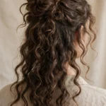 Back view of long wavy curly hair styled in a loose half-up half-down curly bun
